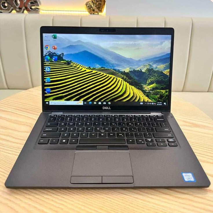 Dell Latitude open showing Windows 10 with mountain landscape wallpaper on wooden desk
